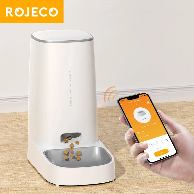 White pet feeder with smartphone app control by ROJECO on a wooden surface.