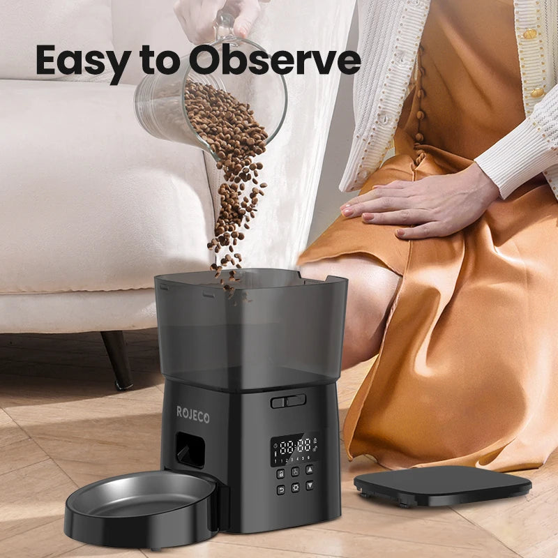 Rojeco coffee grinder with coffee beans being poured into it, placed on a wooden floor.